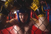 Porträt eines Boxers, der sich an Maschendrahtzaun im Fitnessstudio lehnt — Stockfoto
