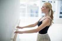 Bailarina estirándose en una barra mientras practica ballet en el estudio - foto de stock