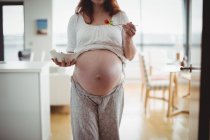 Средняя часть беременной женщины с салатом на кухне дома — стоковое фото