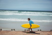 Man carrying surfboard while riding skateboard on beach — Stock Photo