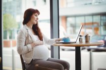 Беременная деловая женщина с ноутбуком в офисной столовой — стоковое фото