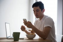 Людина за допомогою мобільного телефону в будинку маючи сніданок — стокове фото