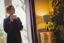 Продумана жінка, дивлячись далеко, маючи каву вдома — стокове фото