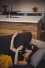 Frau benutzt Virtual-Reality-Headset, während sie zu Hause auf dem Sofa liegt — Stockfoto