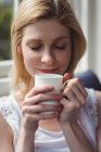 Close-up of beautiful woman smelling coffee in living room at home — Stock Photo