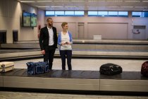 Pareja esperando por equipaje en el área de reclamo de equipaje en el aeropuerto - foto de stock