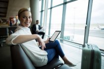 Portrait of female commuter with digital tablet sitting in waiting area at airport — Stock Photo
