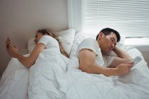 Couple utilisant téléphone portable et tablette numérique dans la chambre à coucher à la maison — Photo de stock