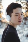 Hombre reflexivo escuchando música en auriculares durante el invierno - foto de stock