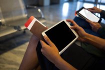 Sección media de la mujer que usa tableta digital en la sala de espera en el aeropuerto - foto de stock