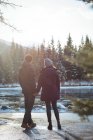 Vue arrière du couple romantique debout au bord de la rivière en hiver — Photo de stock