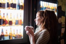 Femme tenant une tasse de café et regardant l'affichage du vin dans le bar — Photo de stock