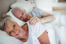 Sorridente coppia anziana sdraiata sul letto in camera da letto — Foto stock