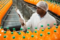 Visão de alto ângulo da área de transferência de leitura do trabalhador masculino ao inspecionar garrafas na fábrica de suco — Fotografia de Stock