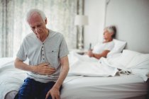 Worried senior man with hand on stomach sitting in bedroom — Stock Photo