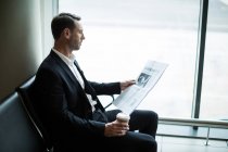 Businessman having coffee while reading newspaper in waiting area at airport — Stock Photo