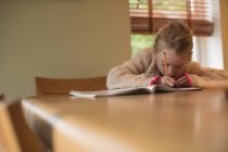 Внимательная девушка делает домашнее задание в гостиной на дому — стоковое фото