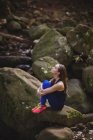 Mujer pensativa sentada en la roca en el bosque - foto de stock