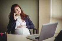Donna d'affari incinta che parla al cellulare in ufficio — Foto stock