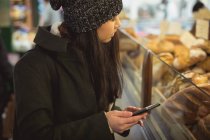 Жінка використовує мобільний телефон біля лічильника хлібобулочних виробів у супермаркеті — стокове фото