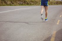 Baixa seção de atleta correndo na estrada do país — Fotografia de Stock