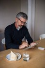 Mann sitzt am Tisch und nutzt digitales Tablet zu Hause — Stockfoto
