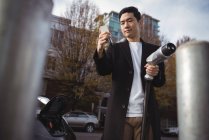 Homme utilisant un téléphone portable tout en tenant le chargeur de voiture à la station de charge du véhicule électrique — Photo de stock
