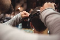 Close-up de homem recebendo cabelo aparado por cabeleireiro com tesoura na barbearia — Fotografia de Stock