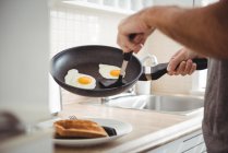 Середній розділ чоловіка збирає смажені яйця з кухонної сковороди на кухні вдома — стокове фото