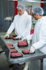 Dois açougueiros embalando carne picada em uma fábrica de carne — Fotografia de Stock