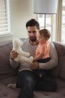 Pai e bebê brincando com ursinho de pelúcia no sofá na sala de estar em casa — Fotografia de Stock
