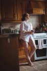 Femme réfléchie tenant tasse de café dans la cuisine à la maison — Photo de stock