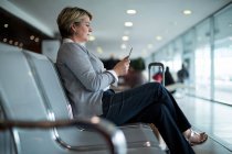 Empresaria que usa teléfono móvil en la sala de espera en la terminal del aeropuerto - foto de stock