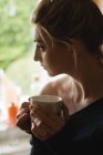 Donna premurosa che tiene una tazza di caffè in cucina a casa — Foto stock