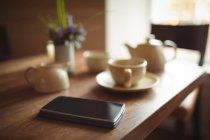 Telefone celular e xícara de café na mesa de madeira no café — Fotografia de Stock