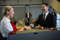 Female staff giving boarding pass to businessman at the check in desk — Stock Photo