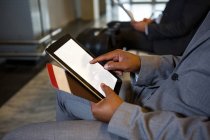 Sección media del hombre de negocios que usa tableta digital mientras está sentado en la terminal del aeropuerto - foto de stock