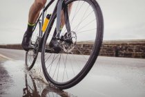 Low section of male athlete riding bicycle on road — Stock Photo