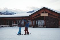 Pareja snowboard mientras alta cincos en la nieve cubierto de campo por casa - foto de stock