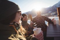 Друзі лижників взаємодіють один з одним, маючи чашки кави на гірськолижному курорті — стокове фото