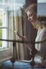 Женщина сидит на кровати и пользуется мобильным телефоном в спальне дома — стоковое фото