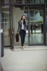 Businesswoman walking while talking on mobile phone near office building — Stock Photo