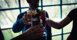 Tres amigos brindando vasos de bebidas en el bar - foto de stock