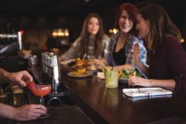 Primer plano del camarero haciendo cóctel con las mujeres hablando en el mostrador del bar — Stock Photo
