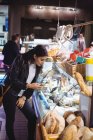 Жінка використовує мобільний телефон, дивлячись на показ їжі в супермаркеті — стокове фото