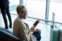 Portrait of female commuter with passport and boarding pass in waiting area at airport — Stock Photo