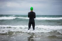 Вид сзади спортсмена, стоящего в море на пляже — стоковое фото