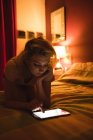 Frau liegend und mit digitalem Tablet auf Bett im Schlafzimmer — Stockfoto