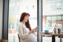 Donna d'affari incinta che utilizza il telefono cellulare in mensa ufficio — Foto stock
