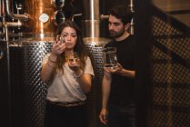 Uomo e donna che esaminano il campione di alcol nella fabbrica di birra — Foto stock